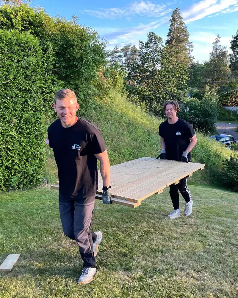 To av montørene i Berg Event bærer en gulvmodul over plenen i kveldssol