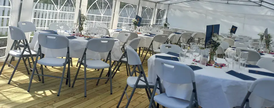 Runde bord med hvite duker og hvite klappstoler på tregulv i et partytelt