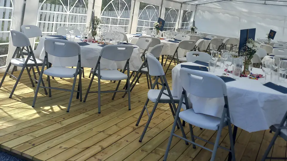 Komfortstoler rundt runde bord med hvite duker på tregulv i et partytelt