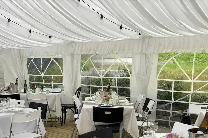 Draperte teltbein mellom vindusveggene i et partytelt med lining i taket og dekkede bord