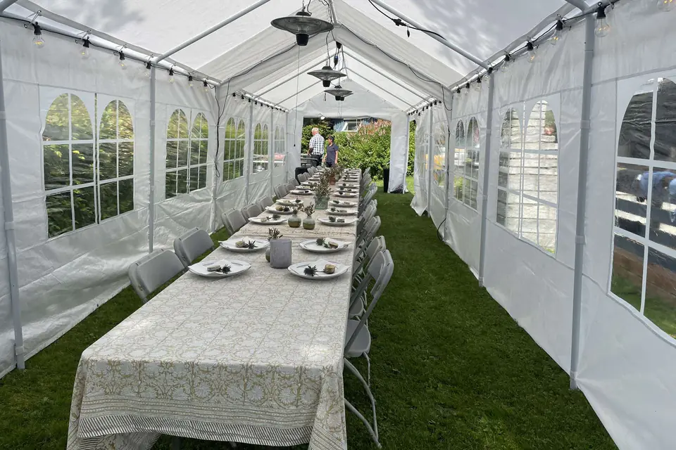 Langbord med mønstret duk dekket gjennom hele det lange, smale partyteltet, med terrassevarmere og lyslenker i taket