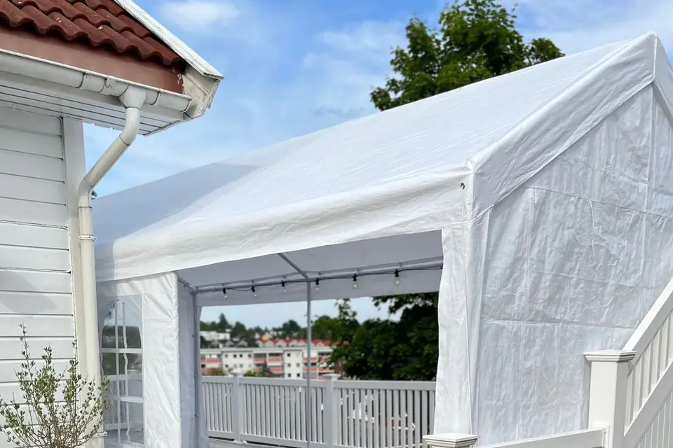 Hvitt partytelt på en terrasse inntil et hvitt trehus, med lyslenke under taket og utsikt gjennom den åpne gavlen