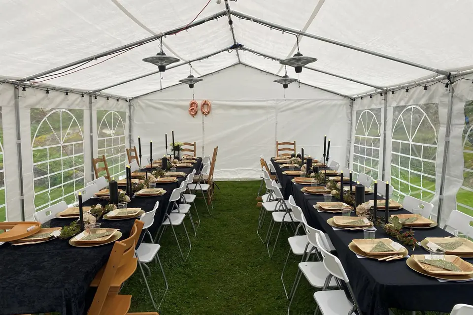 Partytelt med to langbord dekket til 80-årsdag, terrassevarmere i taket og vindusvegger på begge sider