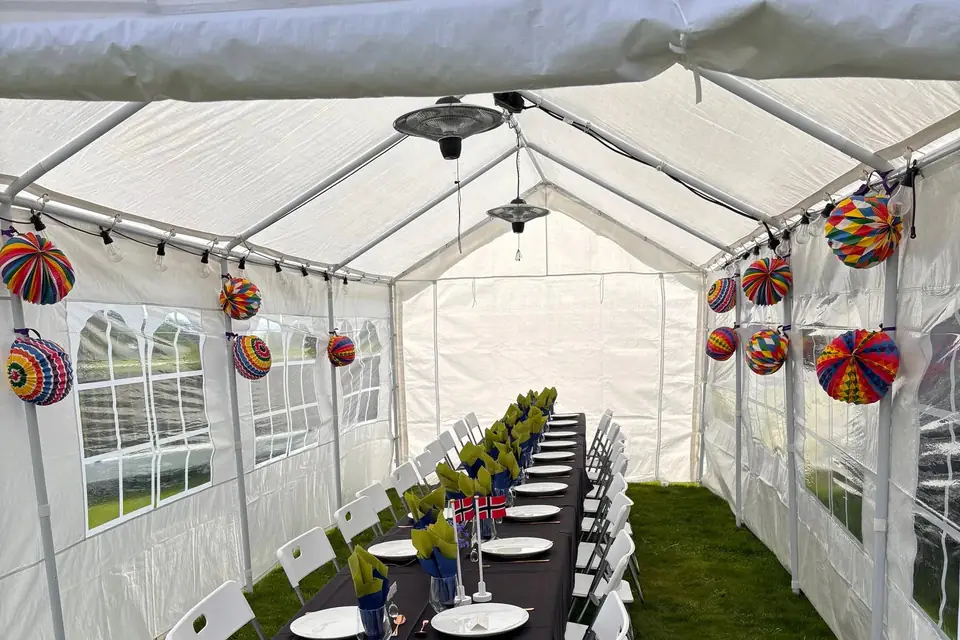 Infravarmere i taket på et partytelt med langbord, fargerike papirlykter og små norske flagg