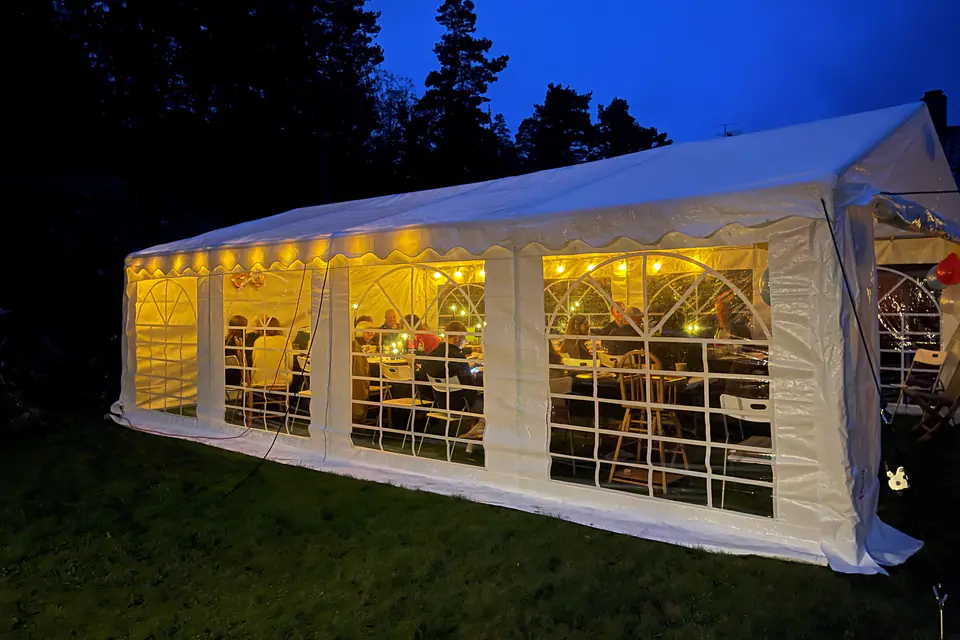 Partytelt i en hage om kvelden, med lysslynger som lyser gjennom vinduene