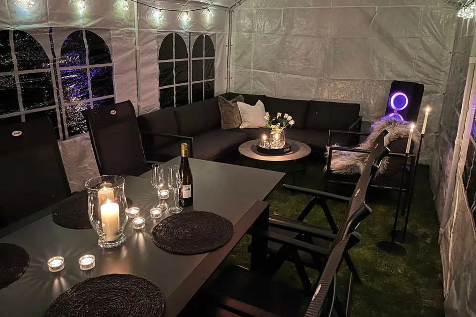 Partytelt om kvelden med lysslynge i taket, levende lys, loungemøbler og en partyhøyttaler med lysring