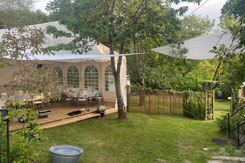 Partytelt på tregulv i en hage, sett gjennom den åpne gavlen, med dekkede bord inne