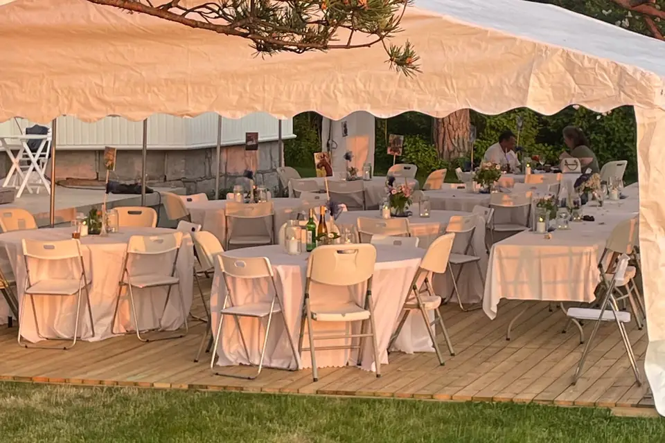 Runde bord med hvite duker på tregulv i et partytelt i kveldssol