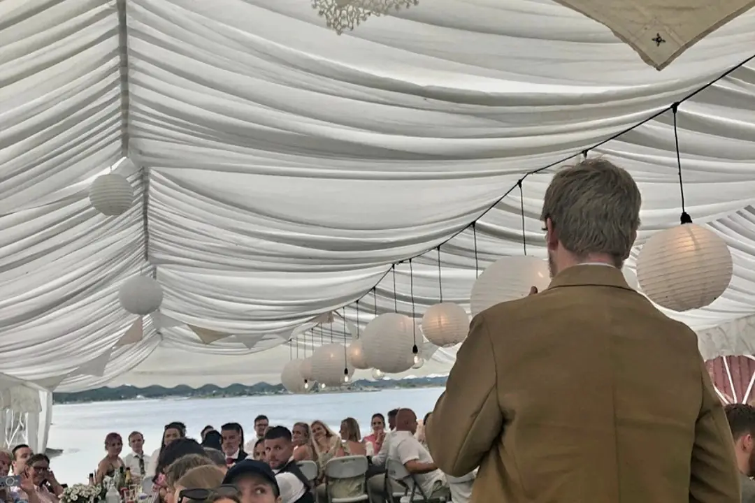 Lining og rislamper i taket på et partytelt, med langbord og sjøen i bakgrunnen