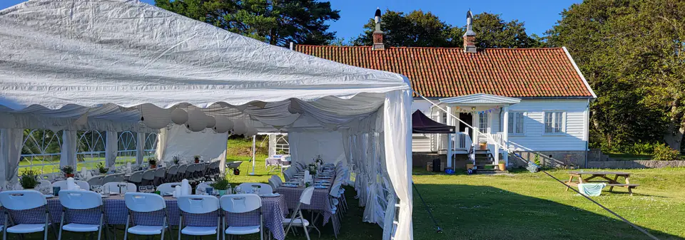 Partytelt med åpen langside og dekkede langbord på en plen ved et hvitt hus, bryllup på Arisholmen