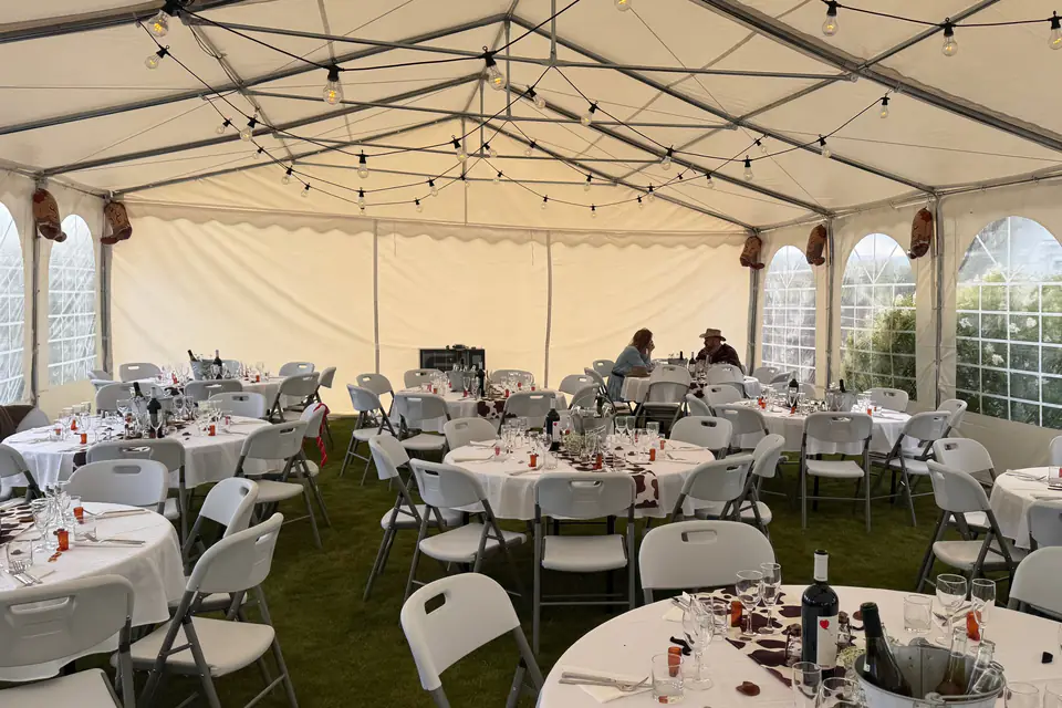 Partytelt dekket til cowboy-fest på Langhus, med runde bord, kumønstrede løpere og lysslynger i taket