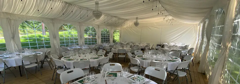 Partytelt dekket til bryllup, med hvit lining i taket, draperte teltbein, tregulv og runde bord med hvite duker