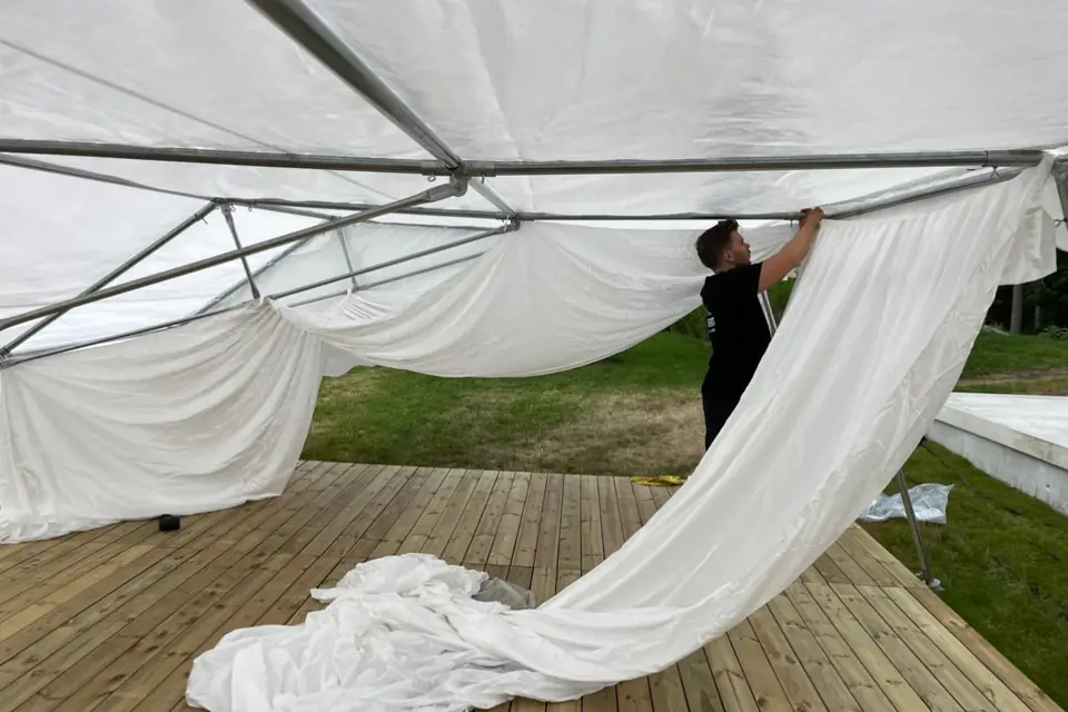 Montør fra Berg Event henger opp lining i taket på et partytelt med tregulv – halve taket er dekket