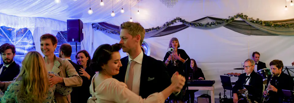Gjester danser til levende musikk i et partytelt med lining i taket og en PA-høyttaler på stativ