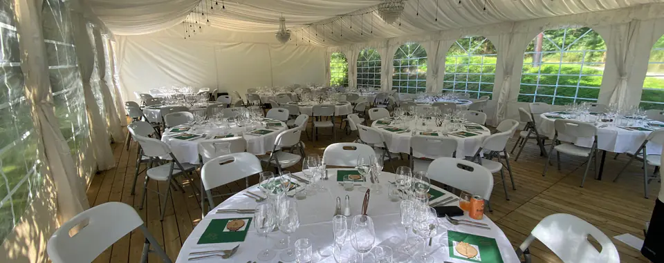 Partytelt dekket til bryllup, med tregulv, lining og lysekroner i taket og runde bord med hvite duker