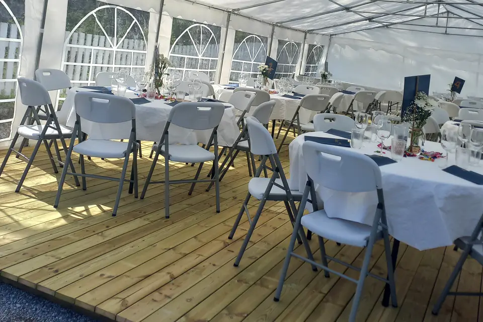 Tregulv i et partytelt med runde bord, hvite duker og klappstoler