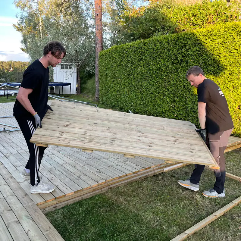 To montører bærer en gulvmodul av impregnerte terrassebord på plass