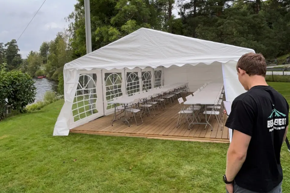 Montør fra Berg Event foran et partytelt med tregulv, langbord og klappstoler