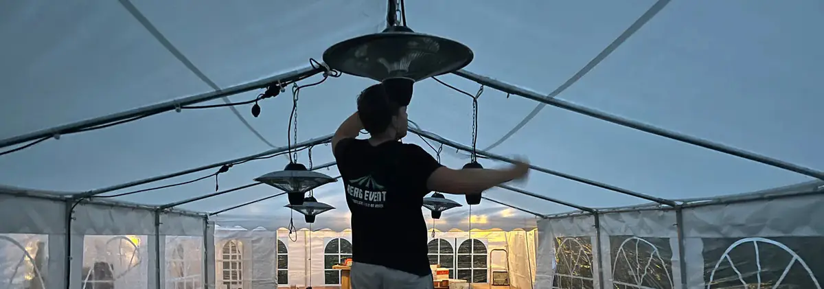 Montør fra Berg Event henger opp infravarmere i taket på et partytelt om kvelden
